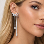 Close-up of a model wearing a bow-shaped silver drop earring with dangling crystals.
