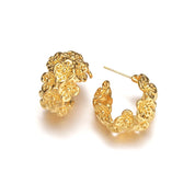A pair of chunky, semi-circular hoop earrings photographed upright on a white background. Each hoop is crafted from stainless steel plated with glossy 18K gold, featuring an embossed design of small buttercup flowers densely covering the outer surface. The hoops are approximately 2.4 cm tall and 1.8 cm wide, with a smooth, reflective finish. They weigh around 15 g and appear waterproof and tarnish-resistant, making them an everyday-ready, statement floral accessory.