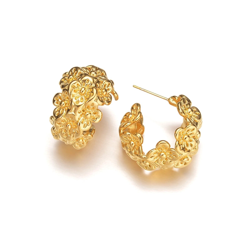 A pair of chunky, semi-circular hoop earrings photographed upright on a white background. Each hoop is crafted from stainless steel plated with glossy 18K gold, featuring an embossed design of small buttercup flowers densely covering the outer surface. The hoops are approximately 2.4 cm tall and 1.8 cm wide, with a smooth, reflective finish. They weigh around 15 g and appear waterproof and tarnish-resistant, making them an everyday-ready, statement floral accessory.