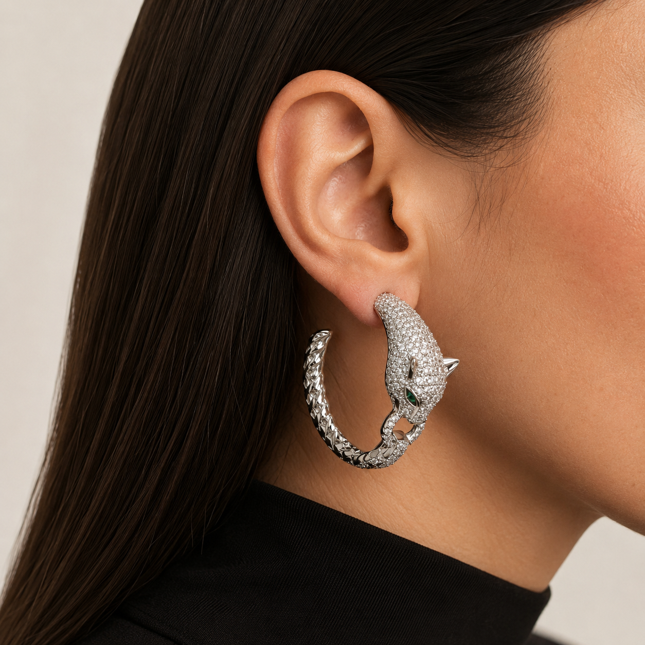 A close-up of a model's ear wearing a large silver hoop earring shaped like a stylized panther head, adorned with small sparkling stones.