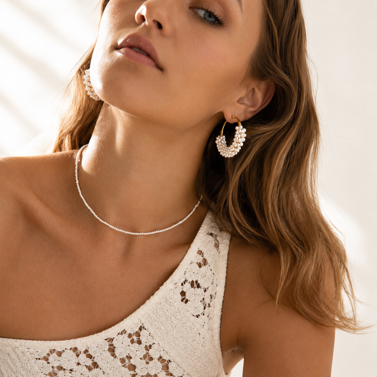 Model wearing a delicate pearl necklace and pearl hoop earrings. 