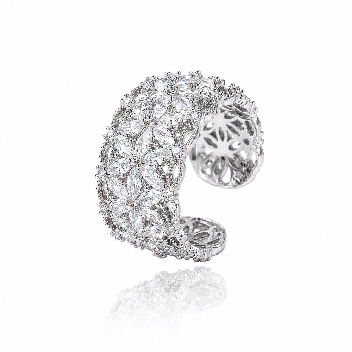 A silver-toned open cuff ring heavily set with clear marquise and round gemstones, shown on a white background with a soft reflection below.