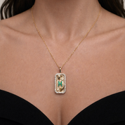 Gold Pisces zodiac necklace with a rectangular pendant featuring a green gemstone and small figure, worn by a person.