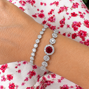 Silver bracelet with a red gemstone on a wrist against a floral background