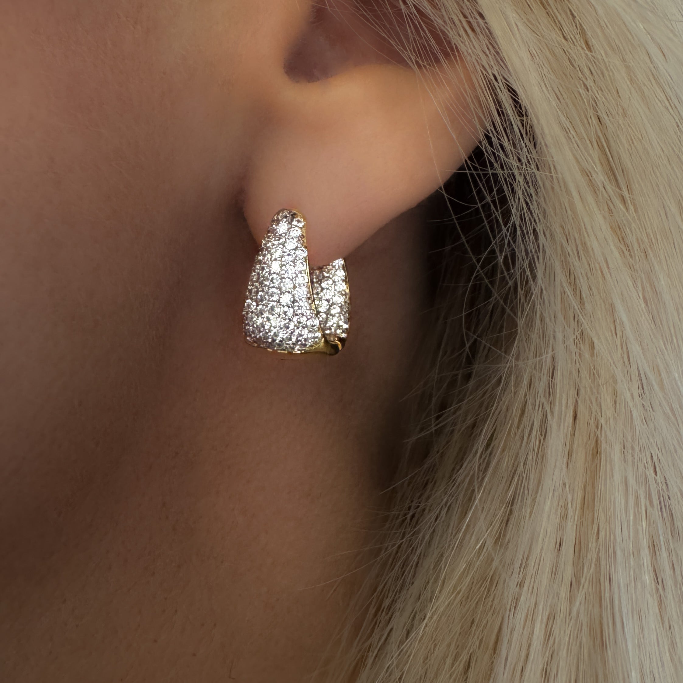 Gold earring with clear stones worn by a person with blonde hair.