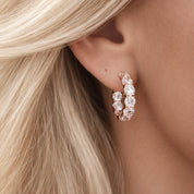 Close-up of a woman wearing a rose gold hoop earring with clear gemstones.