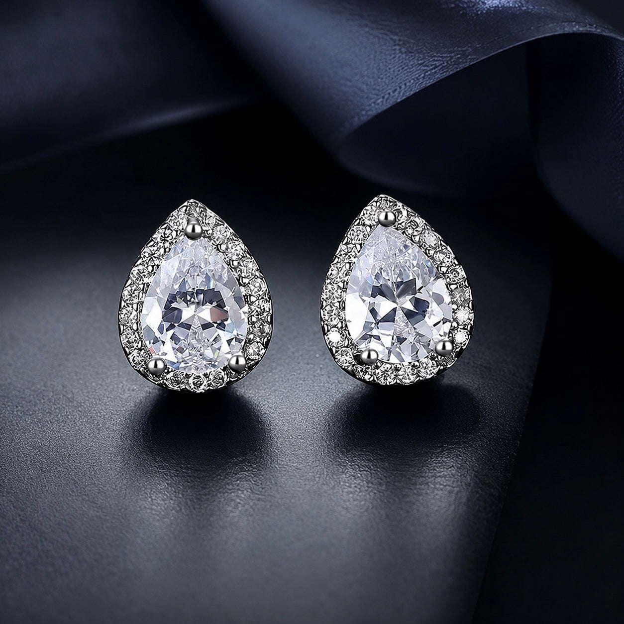 Teardrop-shaped earrings with clear gemstones on a dark fabric background