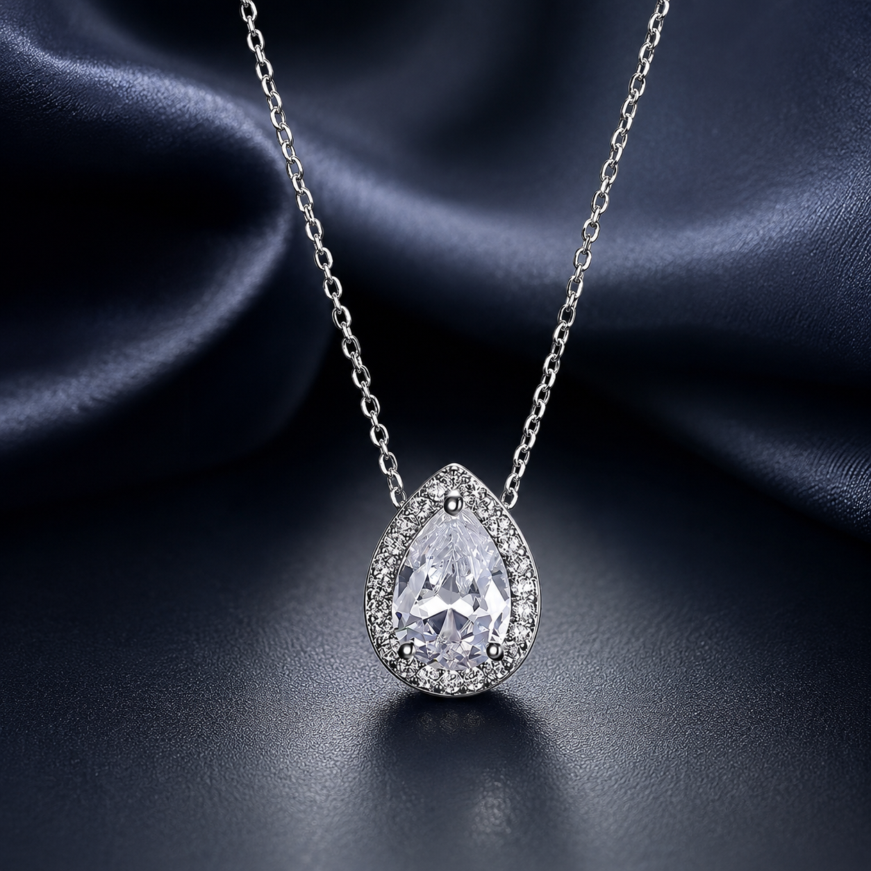 Teardrop-shaped silver pendant on a chain against a dark fabric background
