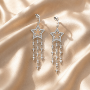 Star-shaped earrings with dangling crystals on a beige fabric background