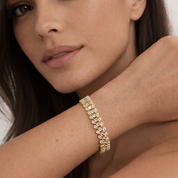 Close-up of a woman's arm wearing a gold bracelet with a neutral background