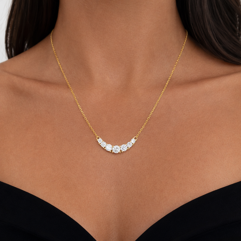 Gold curved bar necklace with round cubic zirconia stones on a delicate chain, shown on a model 
