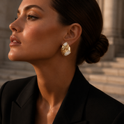 Model wearing gold hammered cz earrings with a blurred architectural background